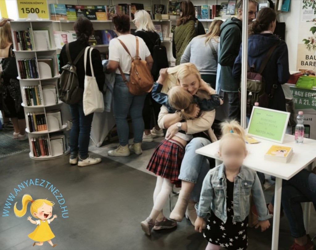 Könyvvásáron három nő és két gyermek látható, akik egy standnál nézelődnek és beszélgetnek.